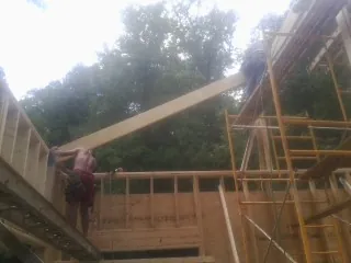 Carpenter raising a rafter beam on a new second story frame in Perry